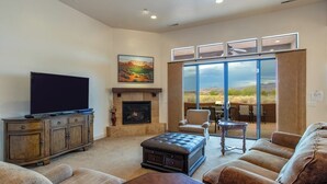 A living room with a fireplace, a television, and a large window offering a view of the outdoors. - Courtyard: Golf + Resort Access + Sand Dunes (Hurricane)