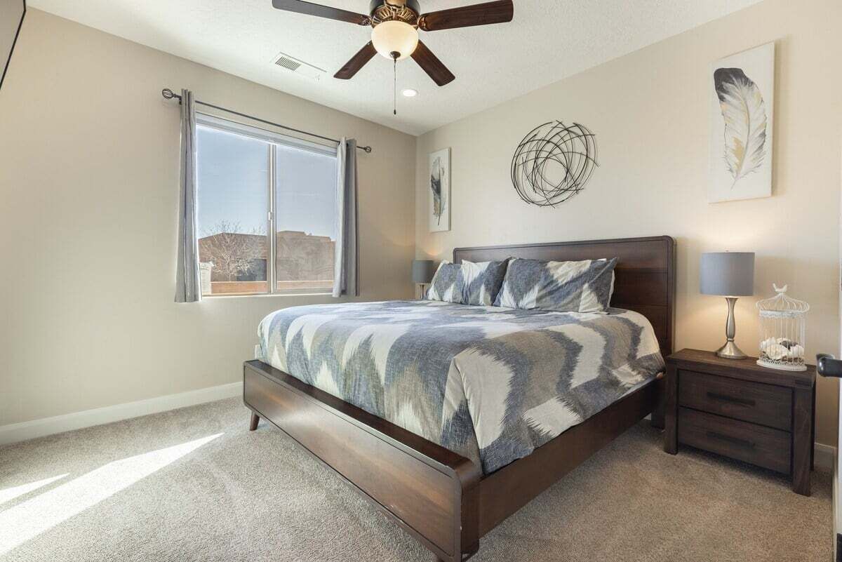 Une chambre à coucher avec un grand lit, un ventilateur de plafond, une fenêtre et une table de chevet avec une lampe.