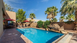Una piscina con borde de piedra, rodeada de palmeras y un patio con mobiliario de exterior.