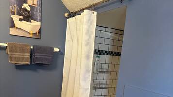 A bathroom with a shower curtain, a towel rack with towels, and a picture on the wall.