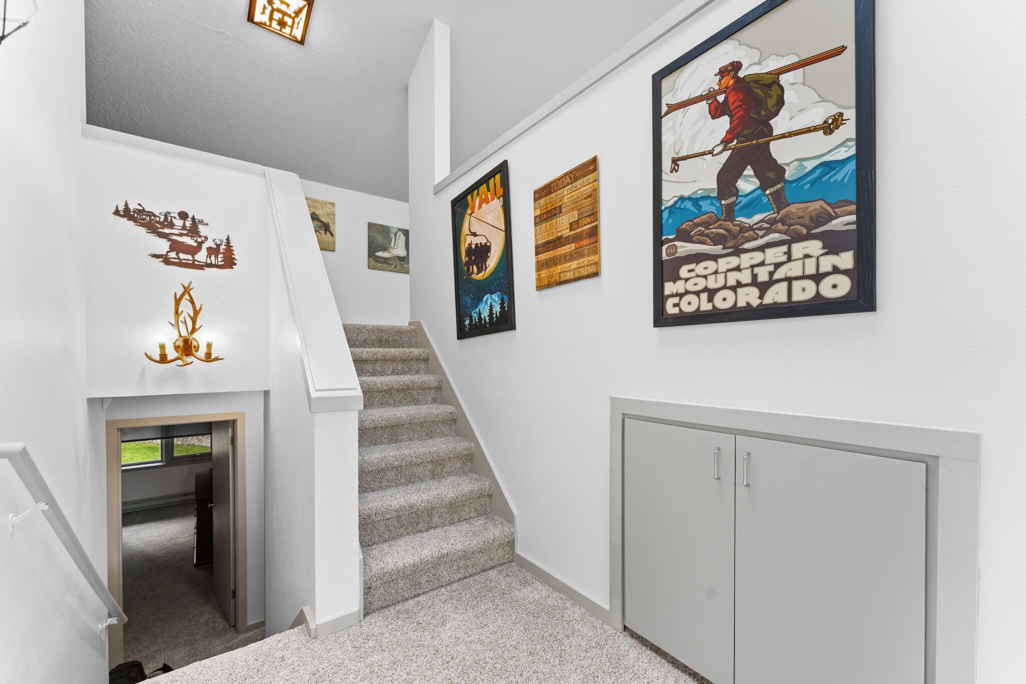 Un escalier recouvert de moquette mène à une porte. Les murs sont blancs et il y a un meuble.