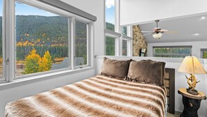 A bedroom with a large window, a bed with striped bedding, a ceiling fan, and a lamp on a wooden table. - L1726-5 (Keystone)