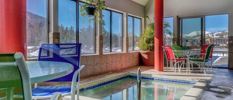 An indoor pool area with a view of mountains, a table with chairs, and a hanging plant.