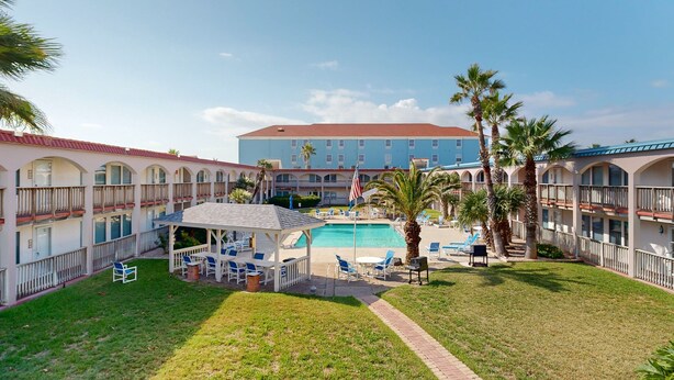 A hotel courtyard with a swimming pool, outdoor seating, and palm trees. - Beach Access Across the Street, Shared Heated Pool (Corpus Christi)
