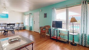 A living room with a wooden floor, a glass coffee table, a television on a stand, and a dining area with chairs and a table. - Beach Access Across the Street, Shared Heated Pool (Corpus Christi)