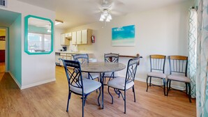 A dining area with a round table and six chairs, a ceiling fan, and a kitchen in the background. - Beach Access Across the Street, Shared Heated Pool (Corpus Christi)
