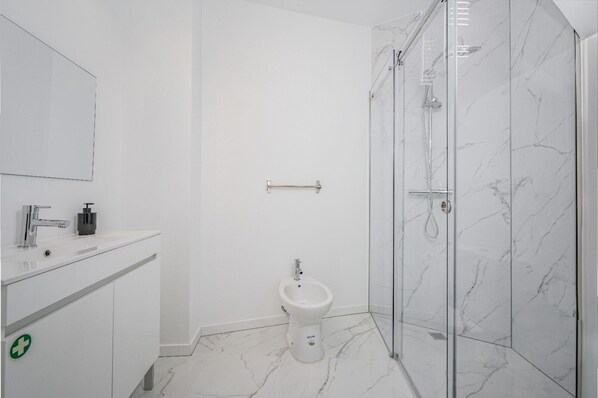 Un baño moderno con inodoro, bidé y zona de ducha con mampara de vidrio.