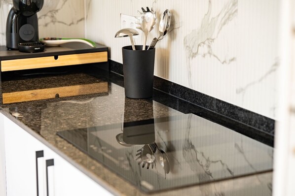 Una encimera de cocina con protector contra salpicaduras de mármol negro, una cafetera y un recipiente negro para utensilios con cubiertos.