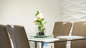 Una mesa de conferencias con un centro de mesa de vidrio que contiene flores blancas y hojas verdes, rodeada de sillas tapizadas en marrón.