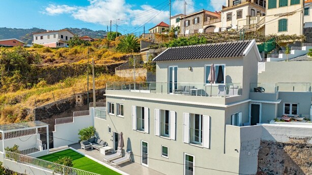 Un edificio moderno de dos pisos con terraza en la azotea, piscina y vista de casas circundantes.