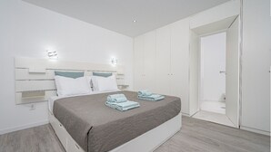 Un dormitorio moderno con una cama grande, paredes blancas y suelo de madera.