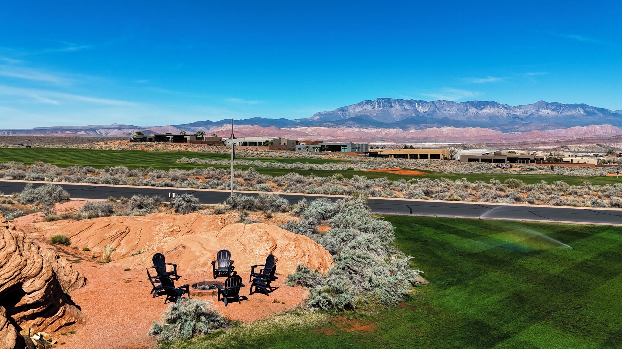 A desert landscape with a large rock formation, a grassy area with chairs, and a building complex in the background.