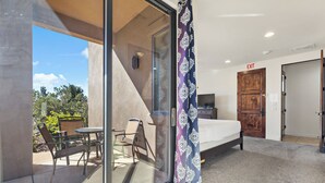 A modern room with a glass door leading to an outdoor seating area, a bed, and an exit sign. - The Sand Castle: Golf View + Sand Dunes + Resort (Hurricane)