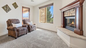 A living room with a fireplace, two armchairs, a stone wall, and a large window. - The Sand Castle: Golf View + Sand Dunes + Resort (Hurricane)