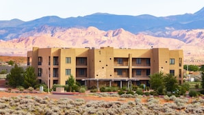 A multi-story building with a flat roof, surrounded by desert vegetation and mountains in the background. - The Sand Castle: Golf View + Sand Dunes + Resort (Hurricane)