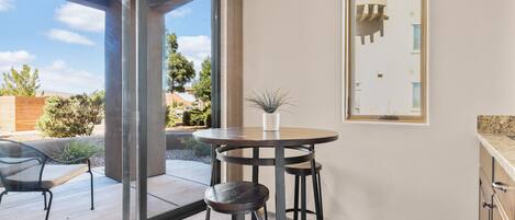 A modern kitchen with a round table and bar stools, large windows, and a view of the outdoors.