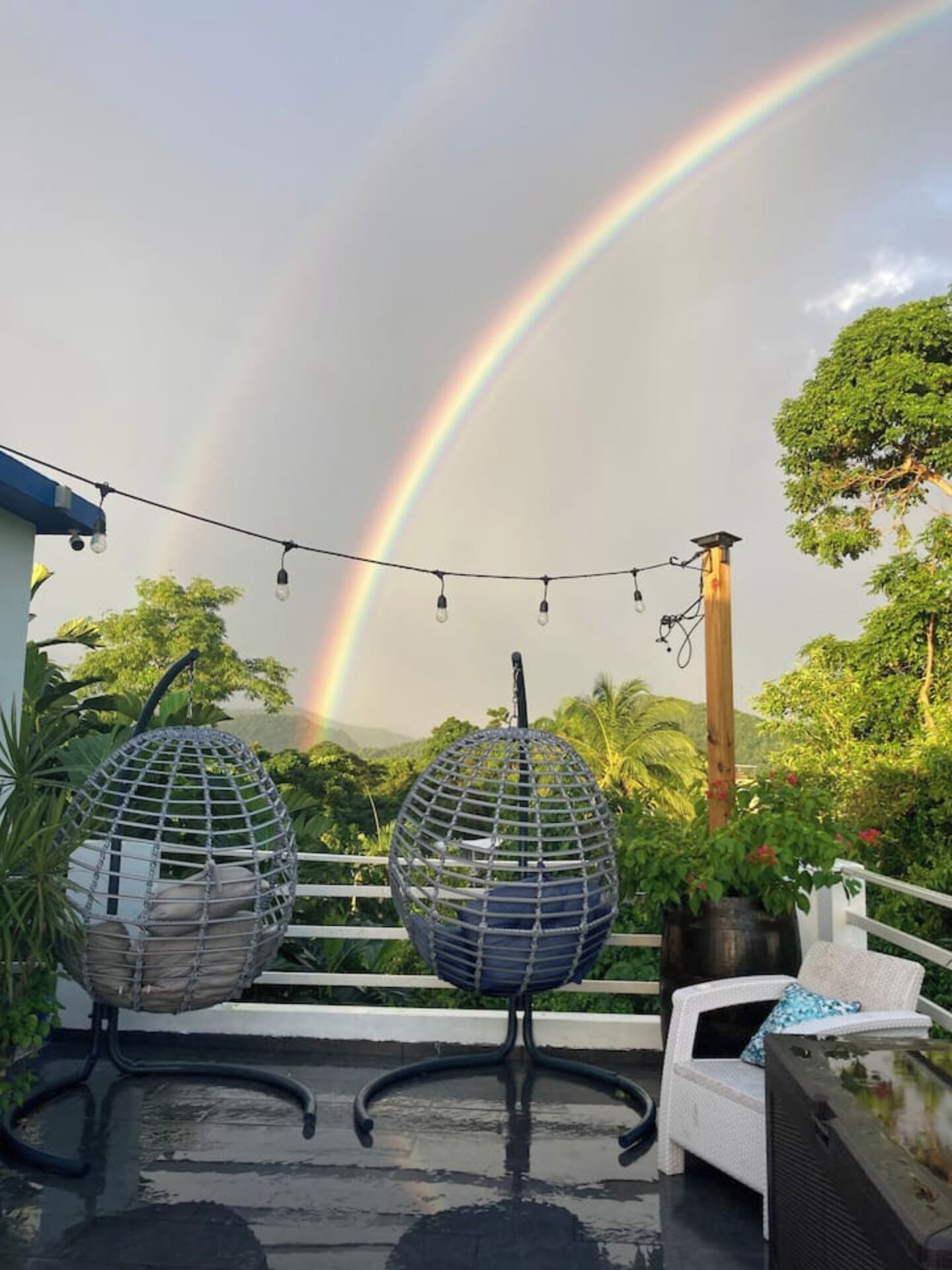 A patio with two spherical hanging chairs, a white chair, and a television on a table. A rainbow is visible in the background.