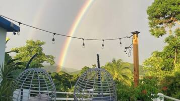 A patio with two spherical hanging chairs, a white chair, and a television on a table. A rainbow is visible in the background.
