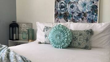 A neatly made bed with a large decorative pillow, a bedside table with a lantern, and a floral painting on the wall.