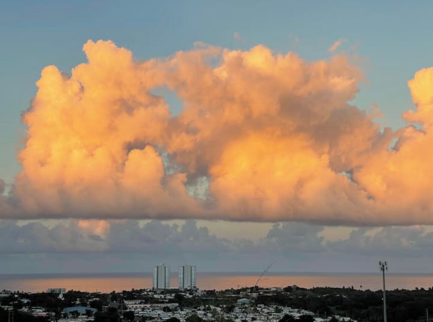 A coastal cityscape with a prominent cloud formation and two high-rise buildings in the distance.