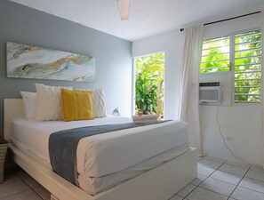 A bedroom with a bed, a window with curtains, a ceiling fan, and a wall-mounted air conditioner. - Tropical Retreat with Spectacular Rooftop Rainforest & Ocean Views With Jacuzzi! (Luquillo)