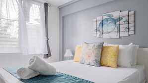 Uma cama bem arrumada com um cobre-leito azul estampado, um par de toalhas enroladas e um quadro de uma tartaruga marinha na parede.