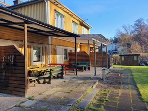 A wooden building with a covered patio area, outdoor seating, and a small shed in a grassy area. - Motel E4 Kolmården (Stavsjö)