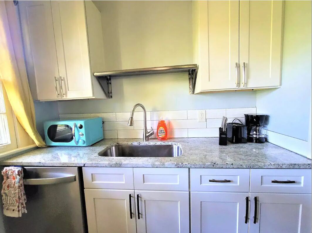 A kitchen with white cabinets, a stainless steel sink, a microwave, and a coffee maker.