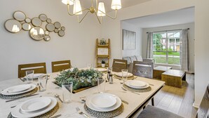 A dining area with a table set for four, a chandelier, wall-mounted mirrors, and a view of the outdoors. - Family Home w/ Game Room & Deck in Spring! (Spring)
