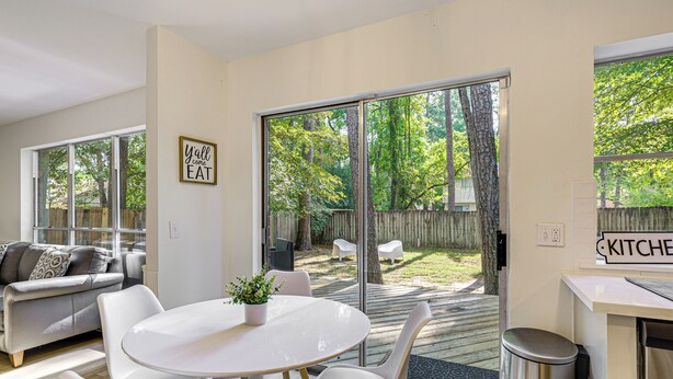 A modern living room with a dining area, large sliding glass doors leading to a backyard, and a kitchen area. - Family Home w/ Game Room & Deck in Spring! (Spring)