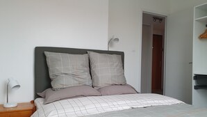 Ein ordentlich gemachtes Bett mit einer grau-weißen Karomusterausstattung, zwei Kissen und einem Nachttischchen mit Lampe.