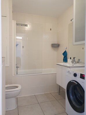 Ein modernes Badezimmer mit Toilette, Badewanne und Waschmaschine.