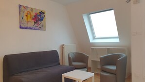 Ein modernes Wohnzimmer mit einem grauen Sofa, einem weißen Couchtisch und zwei grauen Sesseln. Es gibt ein Oberlicht und eine Heizung an der Wand.