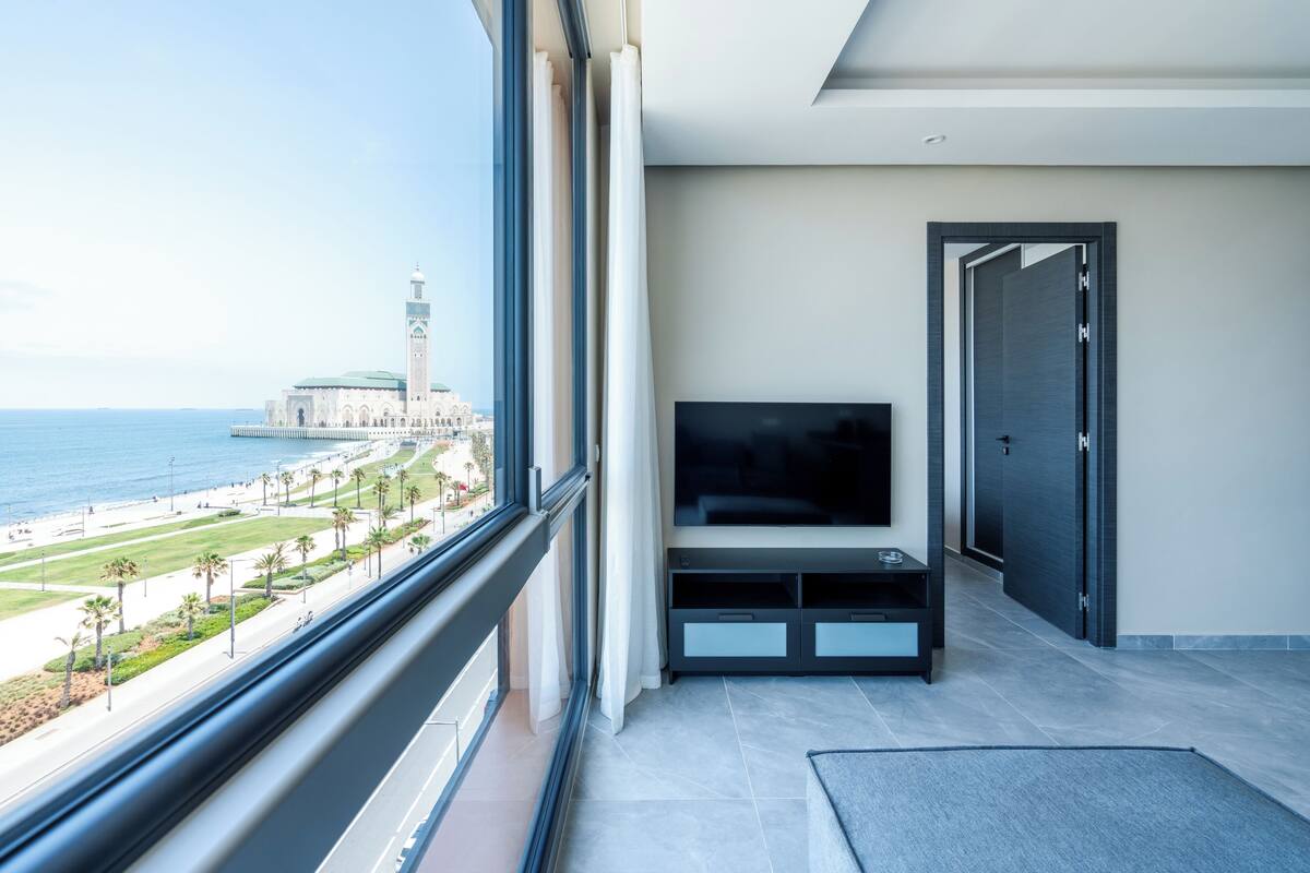 Ein modernes Hotelzimmer mit einem großen Fenster und Blick auf Strand und Moschee.