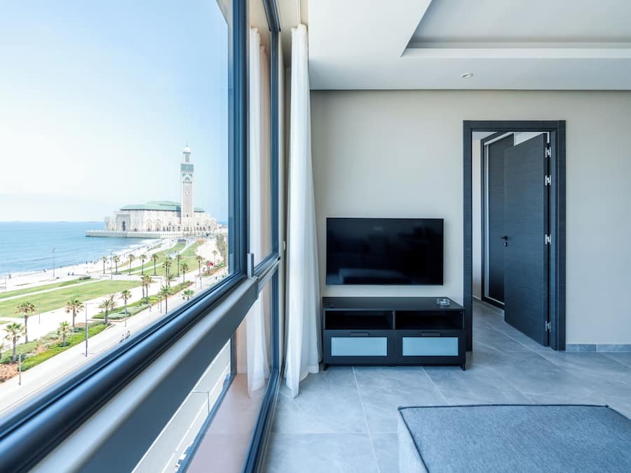 A modern hotel room with a large window offering a view of a beach and a mosque.