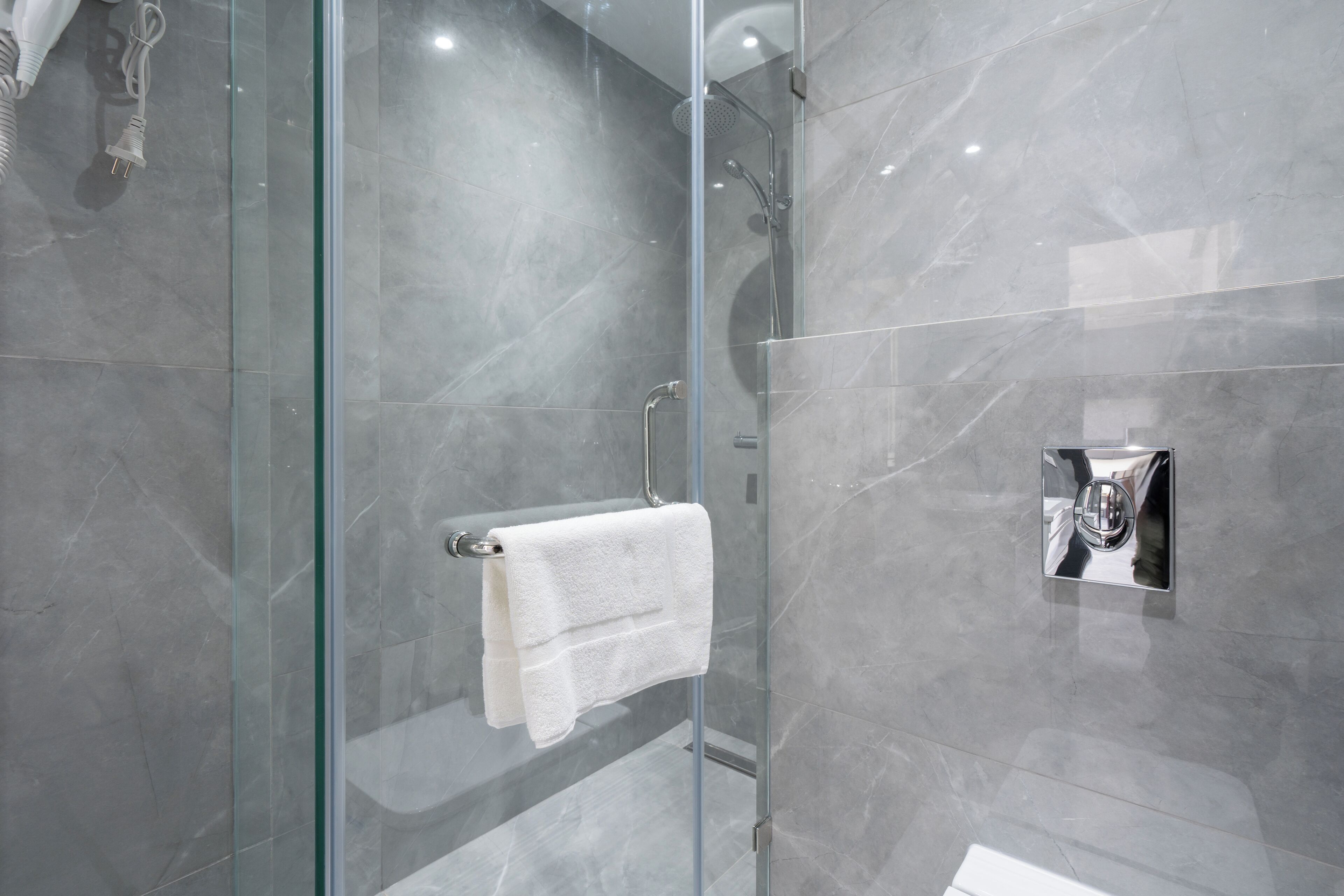 A modern bathroom with a glass-enclosed shower, a white towel hanging on a rack, and a chrome towel warmer.