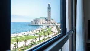 A view of a large mosque with a tall minaret, a waterfront promenade, and palm trees. - Atlantic View Appart'Hotel (Casablanca)