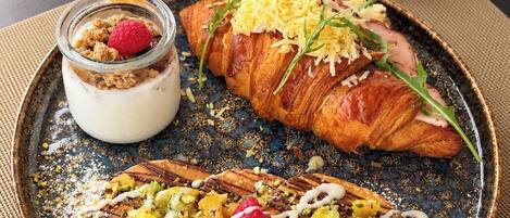 A breakfast setting with a croissant, a fruit-topped crepe, and a glass of orange juice.