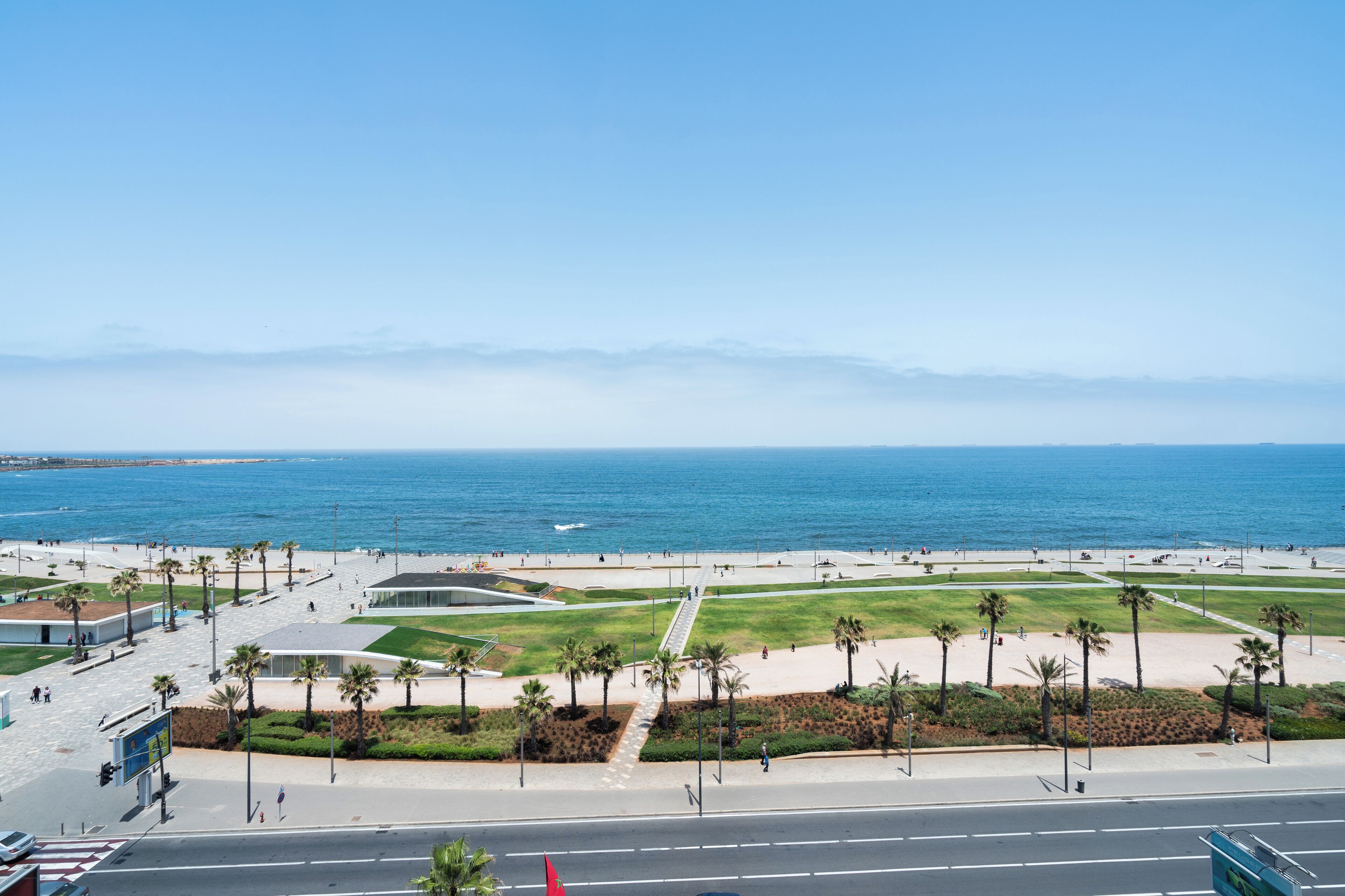A coastal promenade with a view of the ocean, a pedestrian walkway, and palm trees.