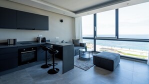 A modern kitchen with a large island, bar stools, and a view of the ocean through large windows. - Atlantic View Appart'Hotel (Casablanca)