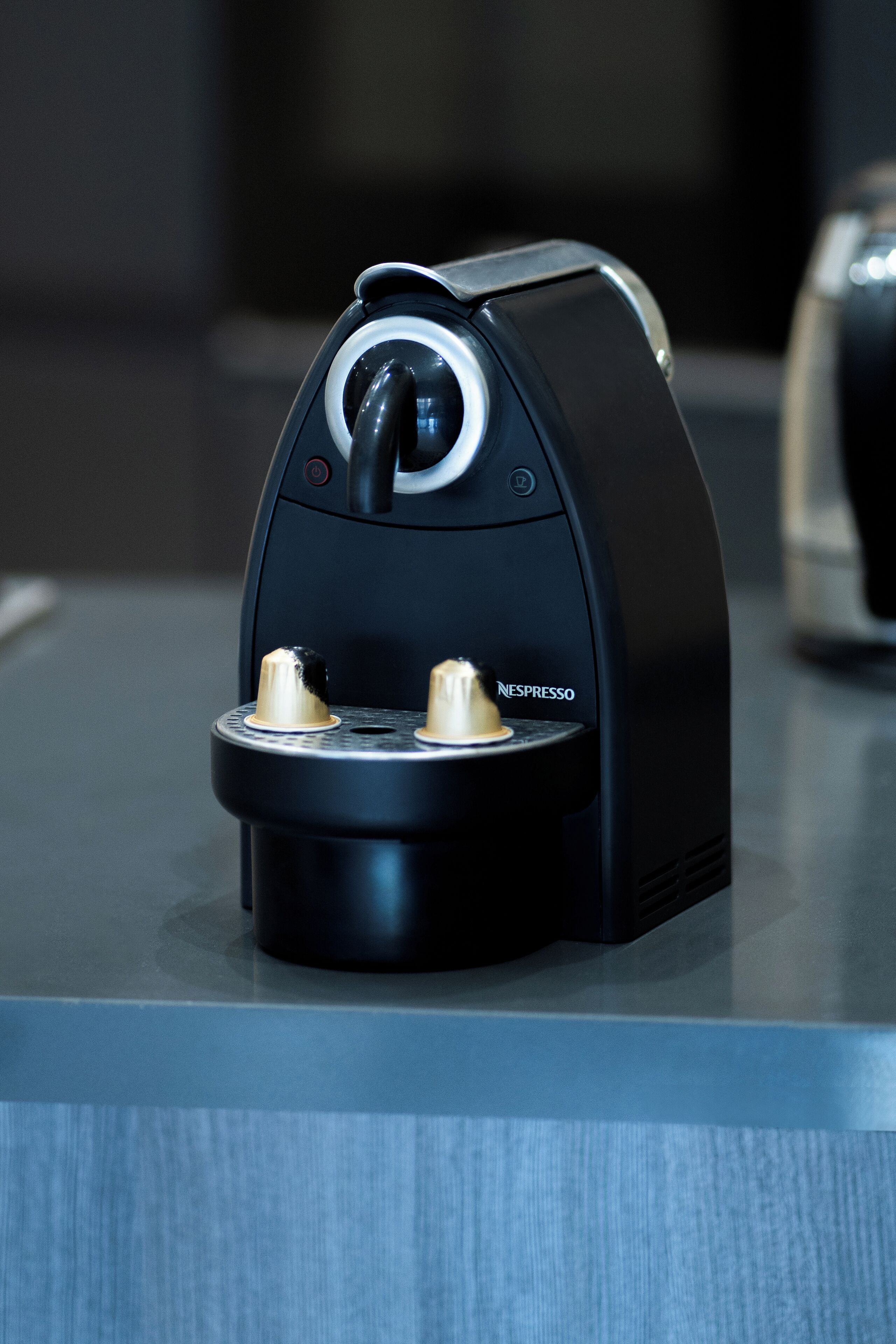 A Nespresso coffee machine with a sleek black design, a digital display, and two coffee capsules.