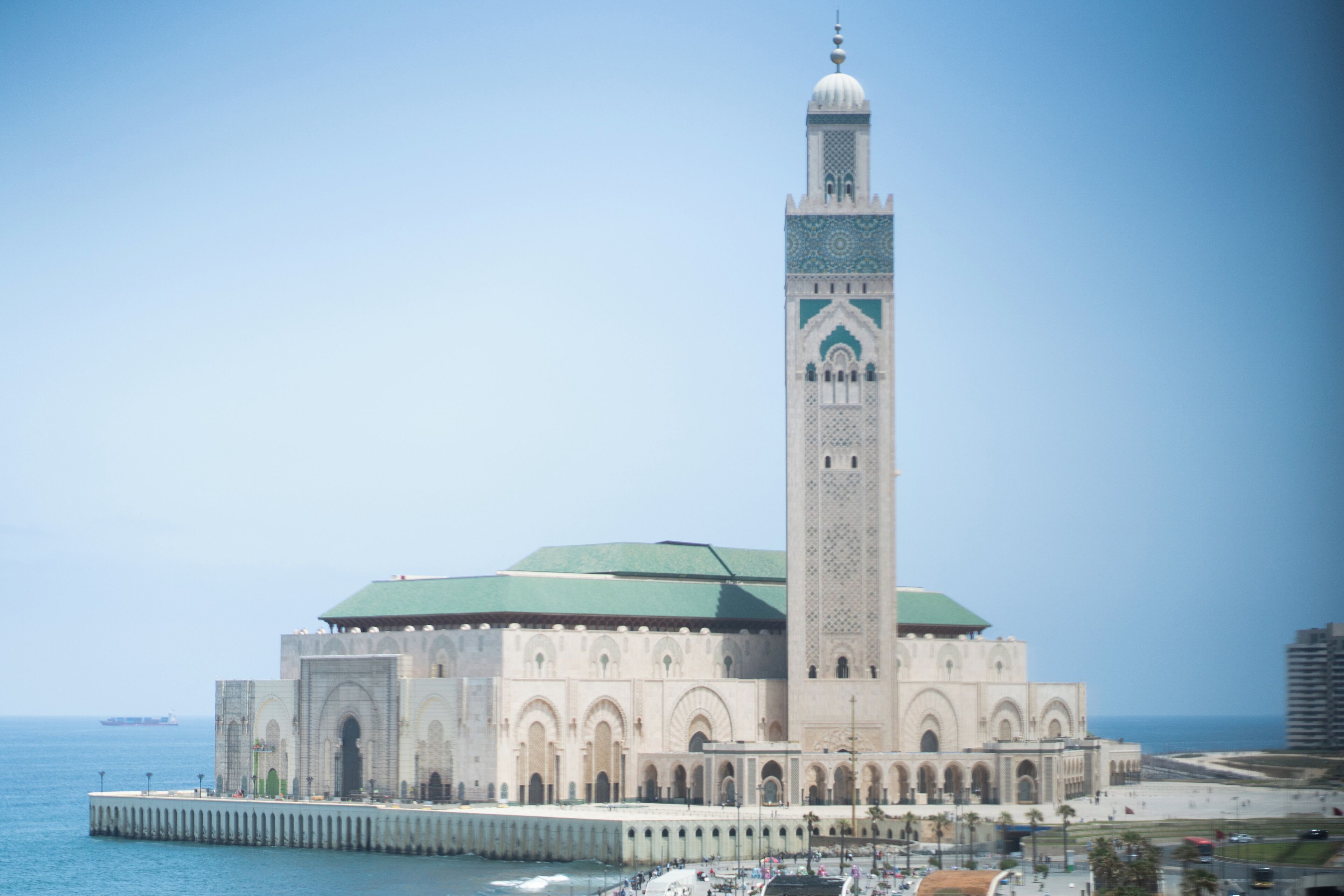 Una gran mezquita con un minarete alto, un techo verde y vistas al agua.