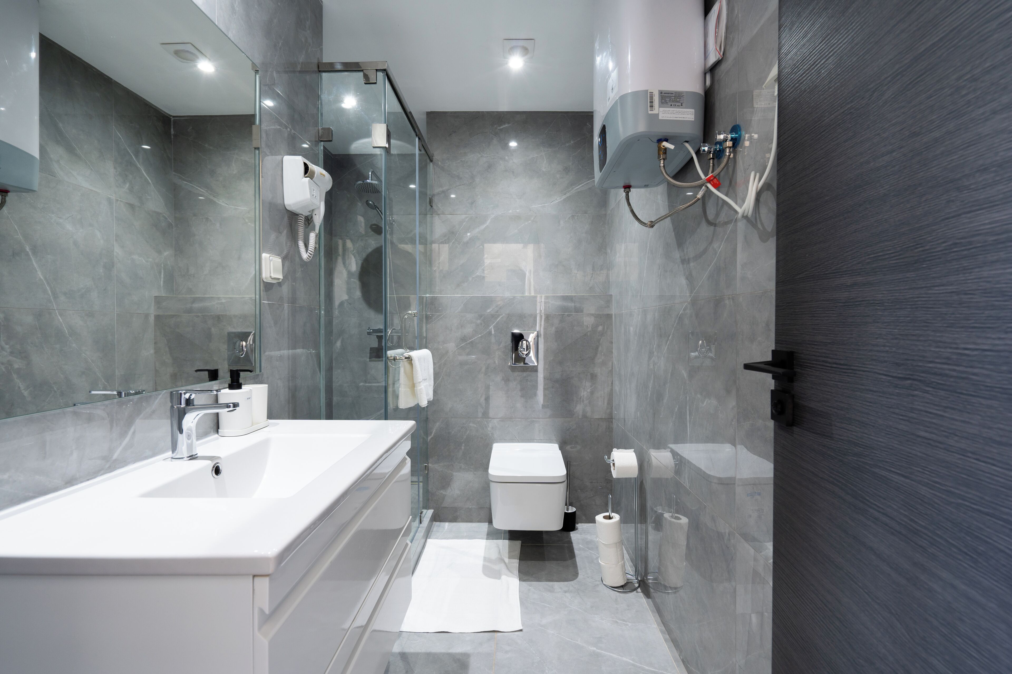 A modern bathroom with a large white sink, a glass-enclosed shower, a toilet, and a towel rack.