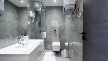 Ein modernes Badezimmer mit einem großen weißen Waschbecken, einer einteiligen Duschkabine, einer Toilette und einem Handtuchhalter.