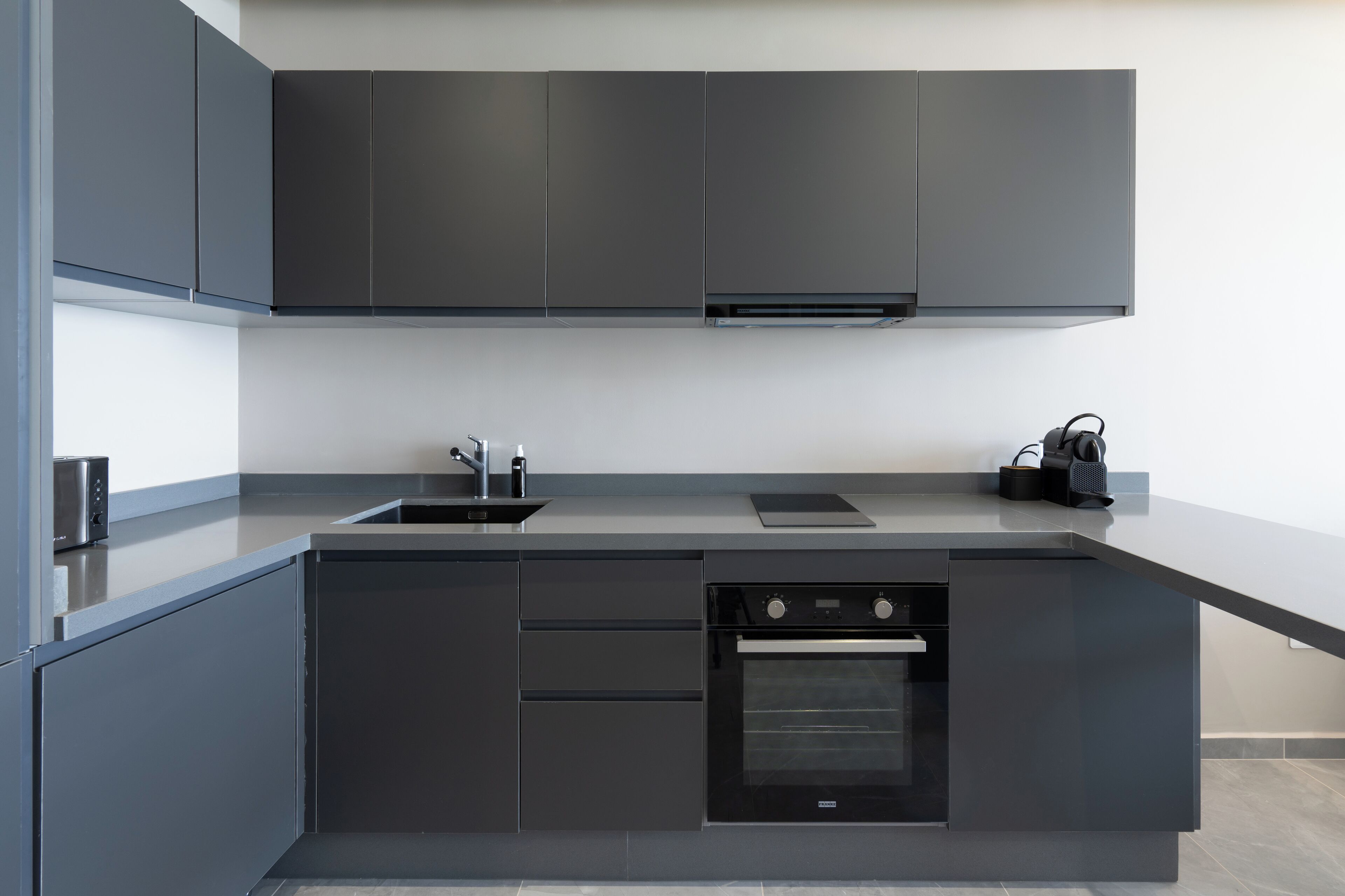 A modern kitchen with dark cabinetry, a built-in oven, and a sink.