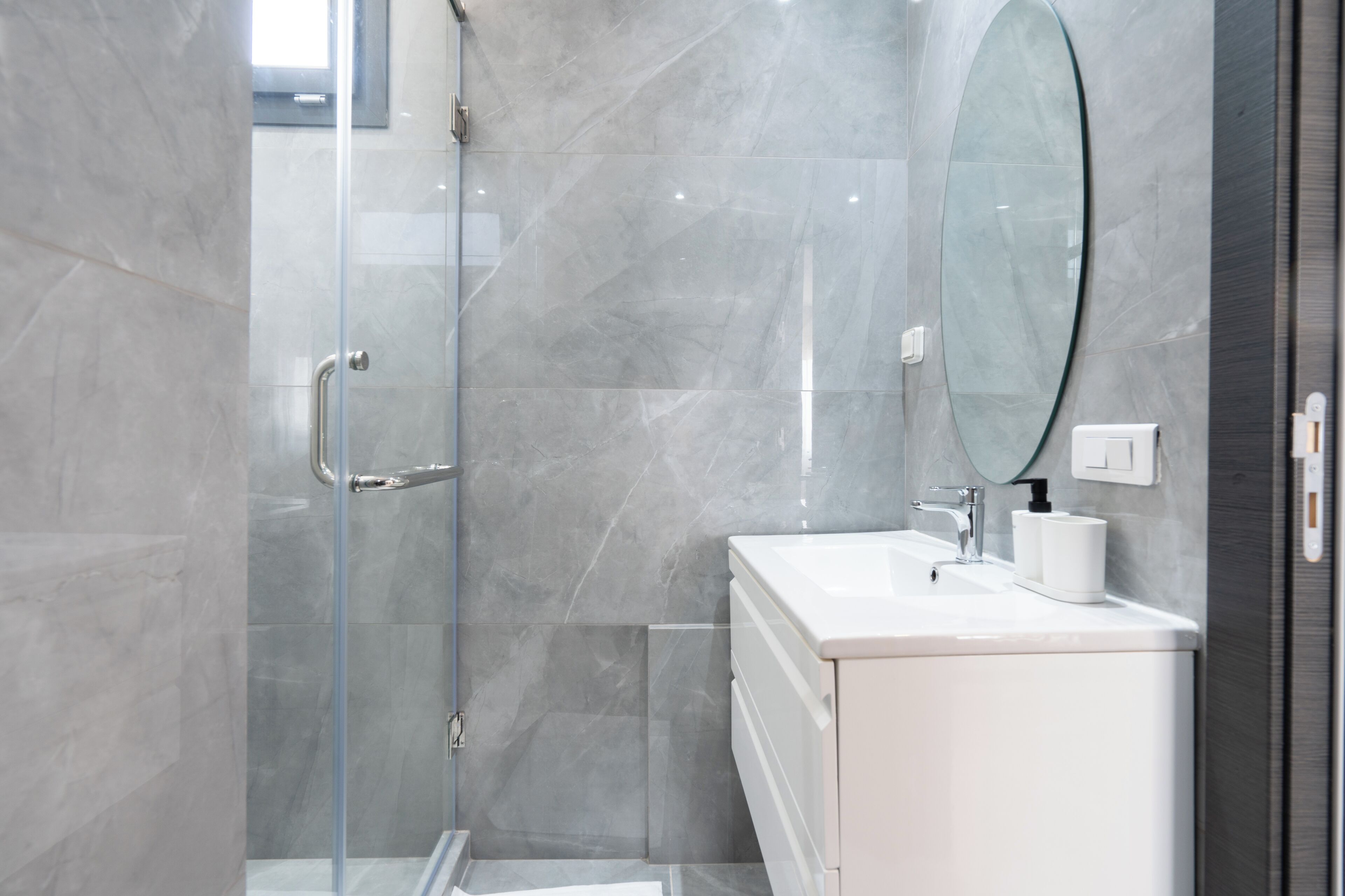 A modern bathroom with a glass shower enclosure, a white sink, and a large mirror.
