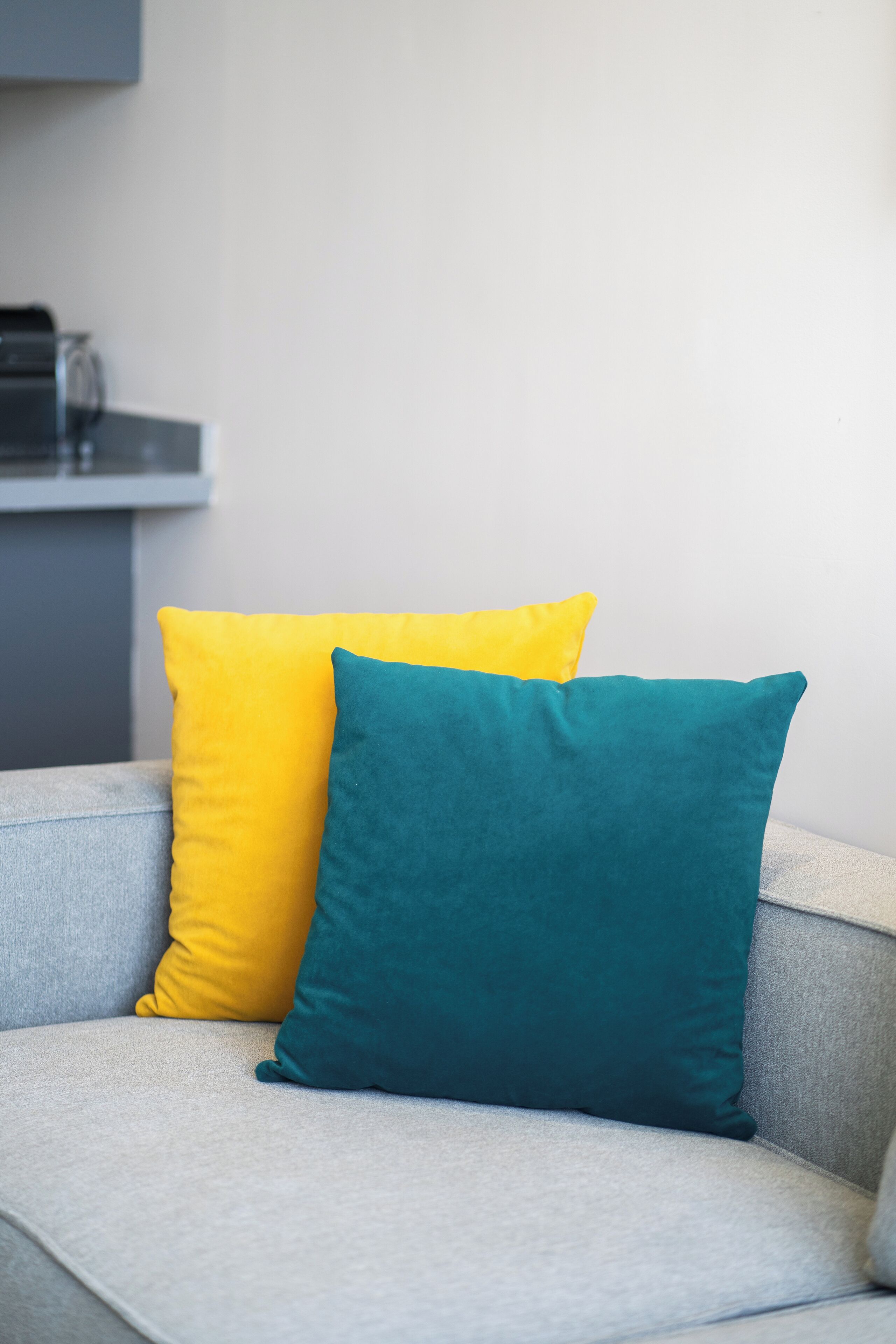 A grey sofa with two cushions, one yellow and one teal.