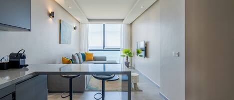 A modern kitchen with a central island, bar stools, and a seating area with a view.