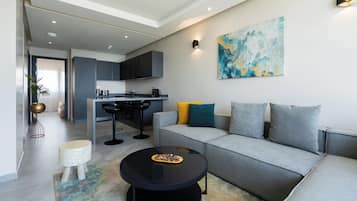 A modern living room with a grey sofa, a round black coffee table, and a kitchen in the background.