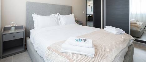 A modern hotel room with a large bed, a bedside table with a lamp, and a mirror reflecting the room.